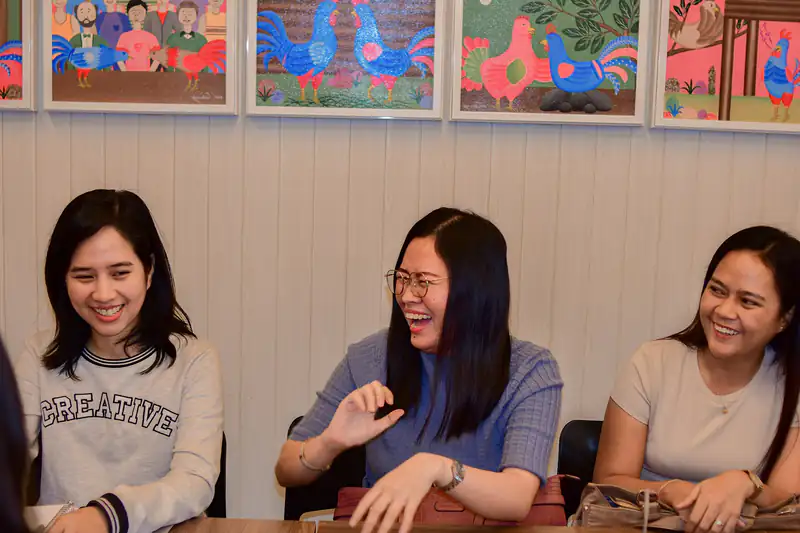 Three young Filipino women laughing together at a table