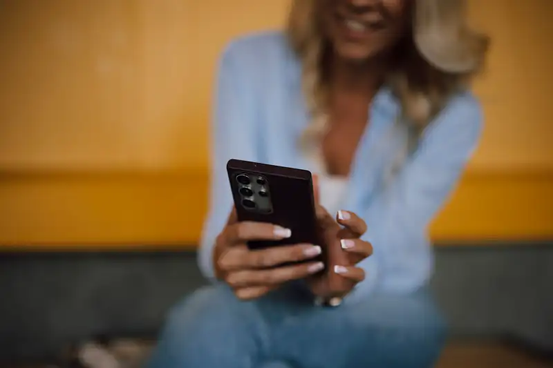A smiling woman with her face blurred holding a smartphone with both hands